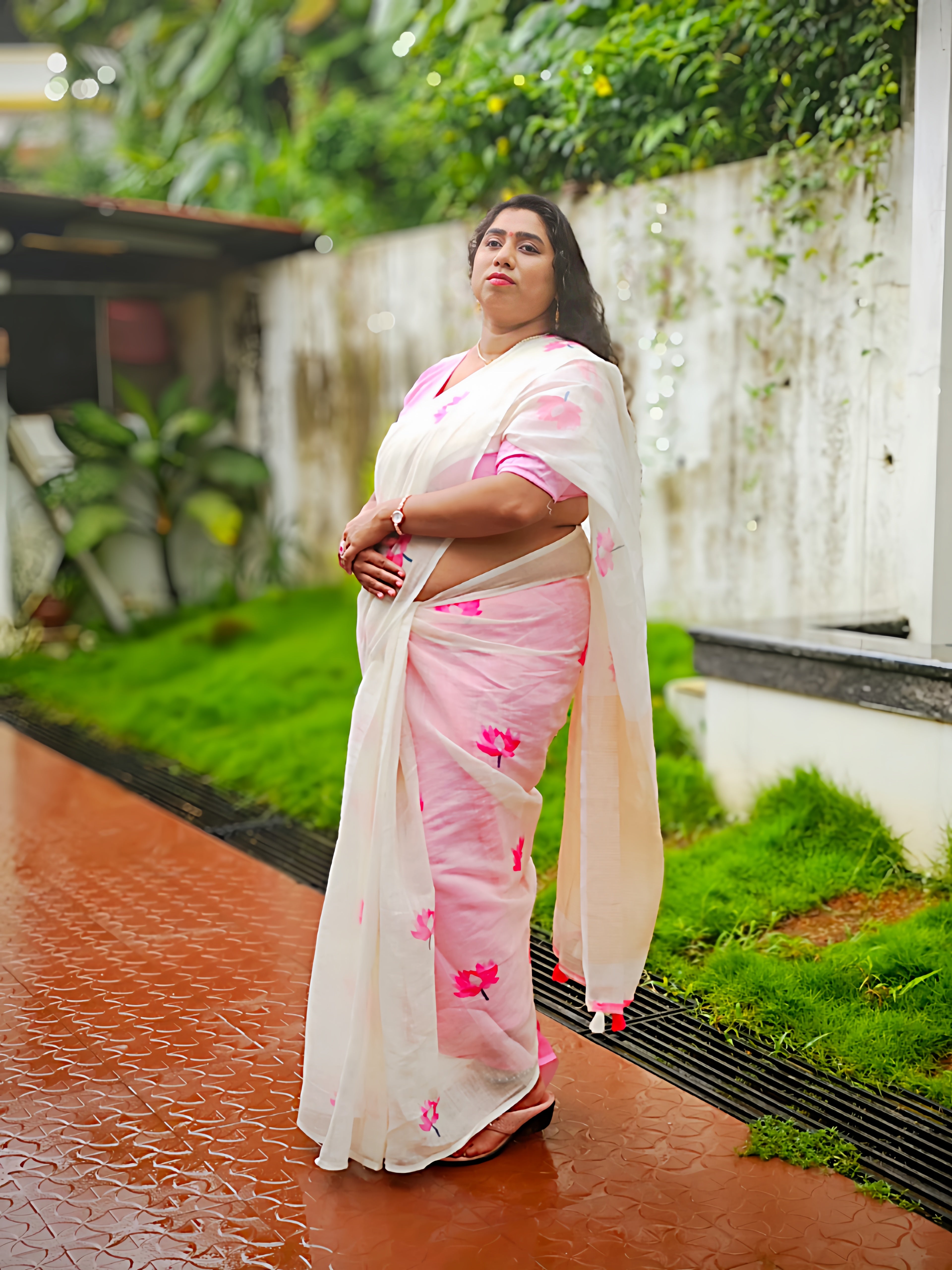 Full-length view of a woman wearing a soft cotton linen white saree with pink lotus floral print and matching pink blouse. Lightweight premium saree for festive, office, casual and everyday wear by Vyra Fashion.
